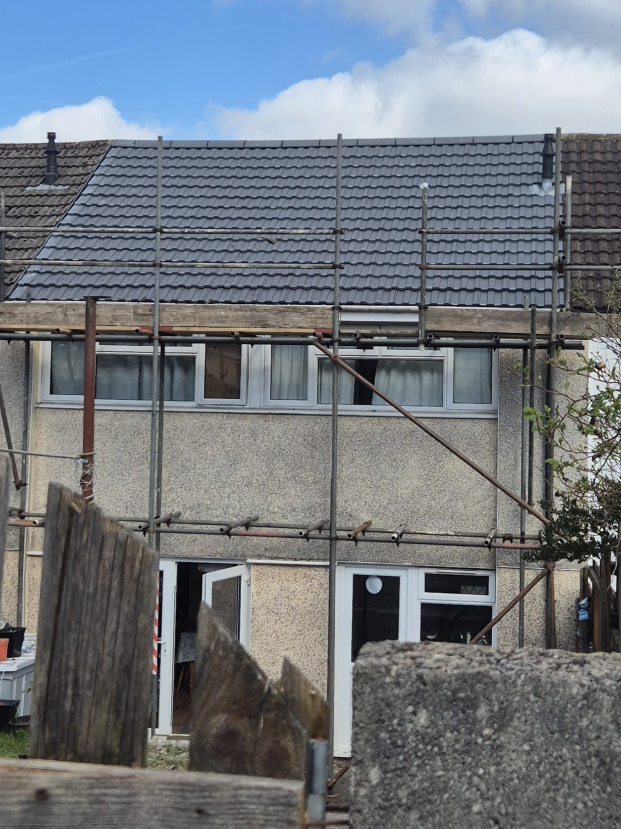 Roof mid-strip with old tiles piled on scaffold